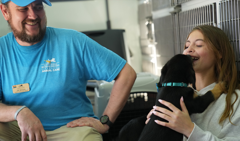 A Humane Society of Naples volunteer introduces a girl to a black adoptable puppy in the adoption truck, while the girl gets kisses from the pup